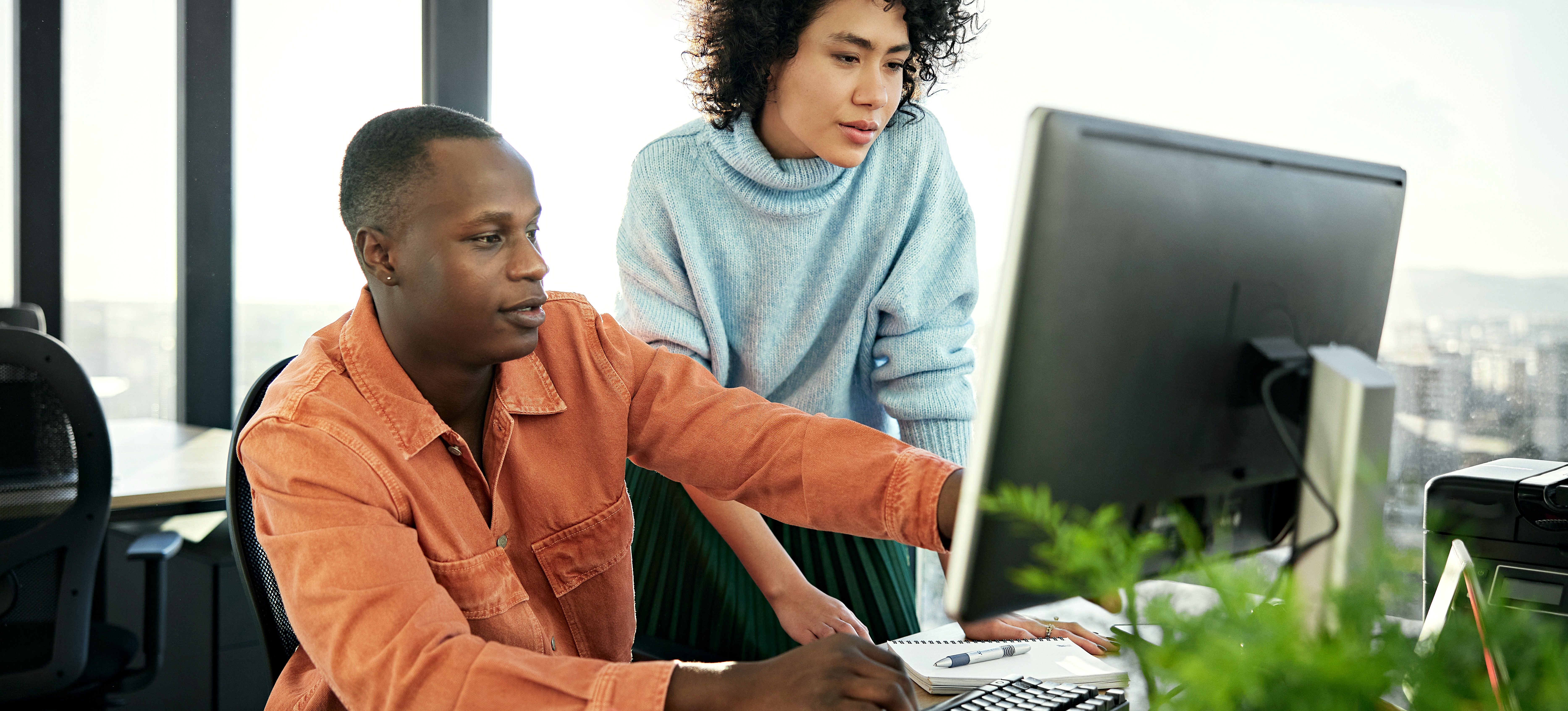 [Image en vedette] Un concepteur UX et un concepteur UI discutent d'un projet de conception web tout en regardant un écran d'ordinateur dans un bureau ensoleillé.
