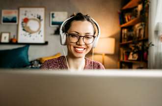 [Featured image] A person in a purple shirt with over-ear headphones and glasses sits in front of a laptop working on ChatGPT.