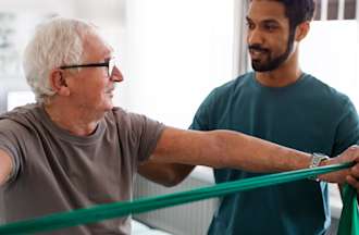 [Featured image] A physical therapist with a degree assists an elderly patient with the help of a resistance band.