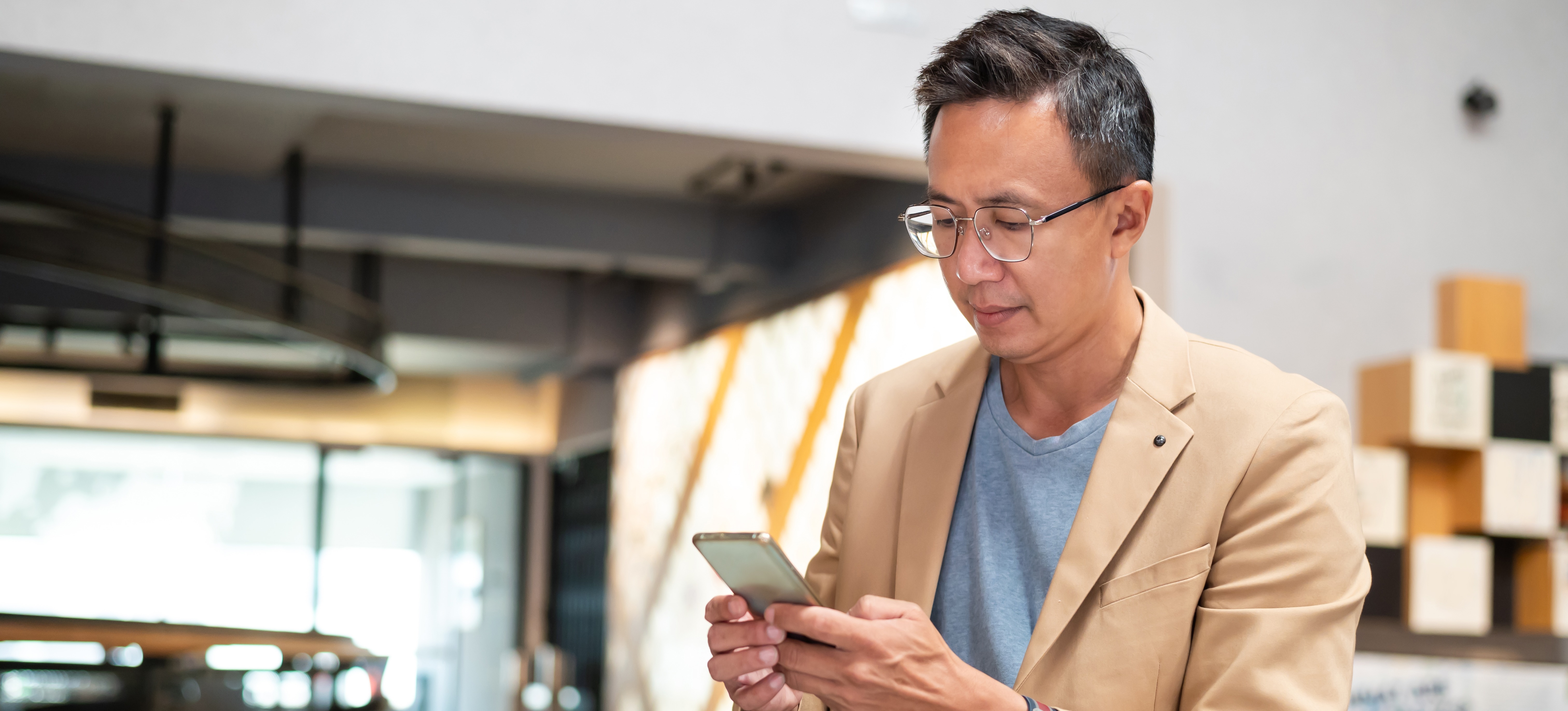 [Image en vedette] Un homme d'affaires vêtu d'un blazer beige et d'une chemise grise consulte avec désinvolture des informations sur l'apprentissage mobile sur son smartphone tout en profitant d'une nouvelle option de développement professionnel.