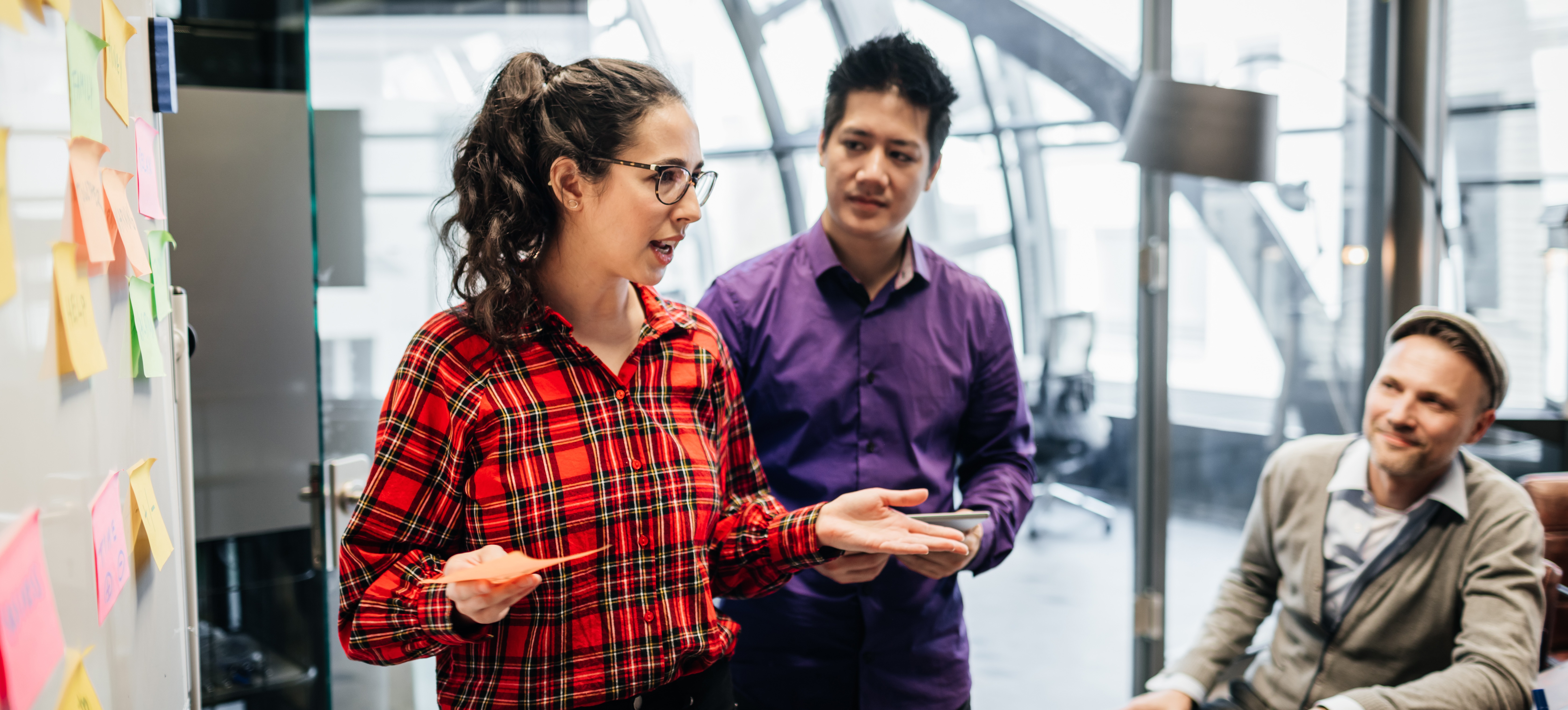 [Featured image: A project manager stands in front of sticky notes on a whiteboard during a daily standup meeting.]
