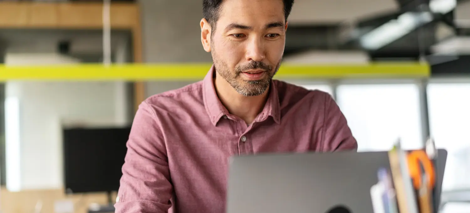 [Featured Image] A person working for an IT manager salary sits in front of his laptop in an office space.
