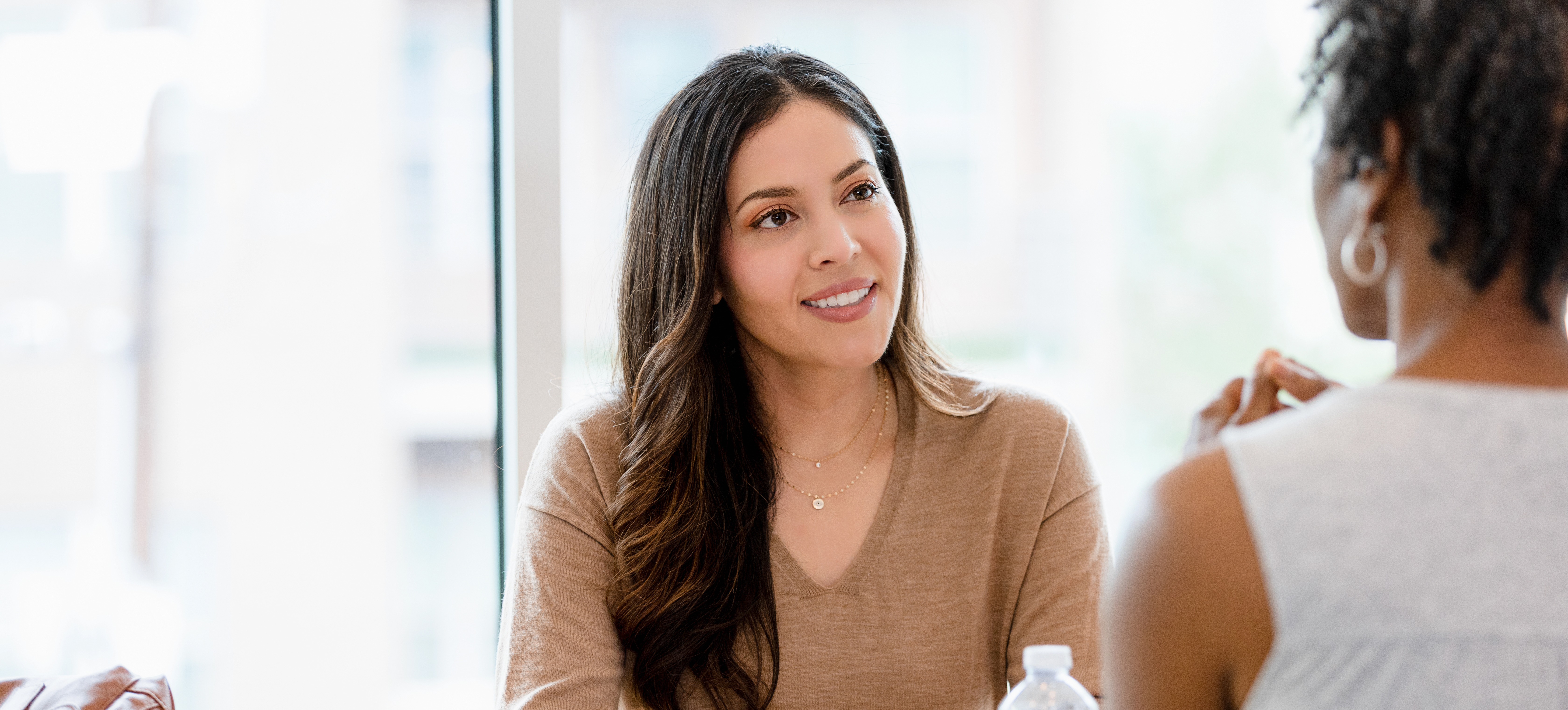 [Featured Image] Two women sit at a table for an interview while the supervisor asks angular interview questions.