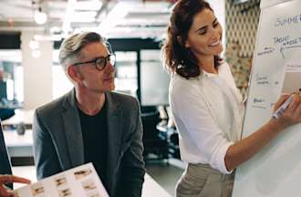 [Featured image] A woman leads her marketing team in defining their target market by building a user persona on a whiteboard.