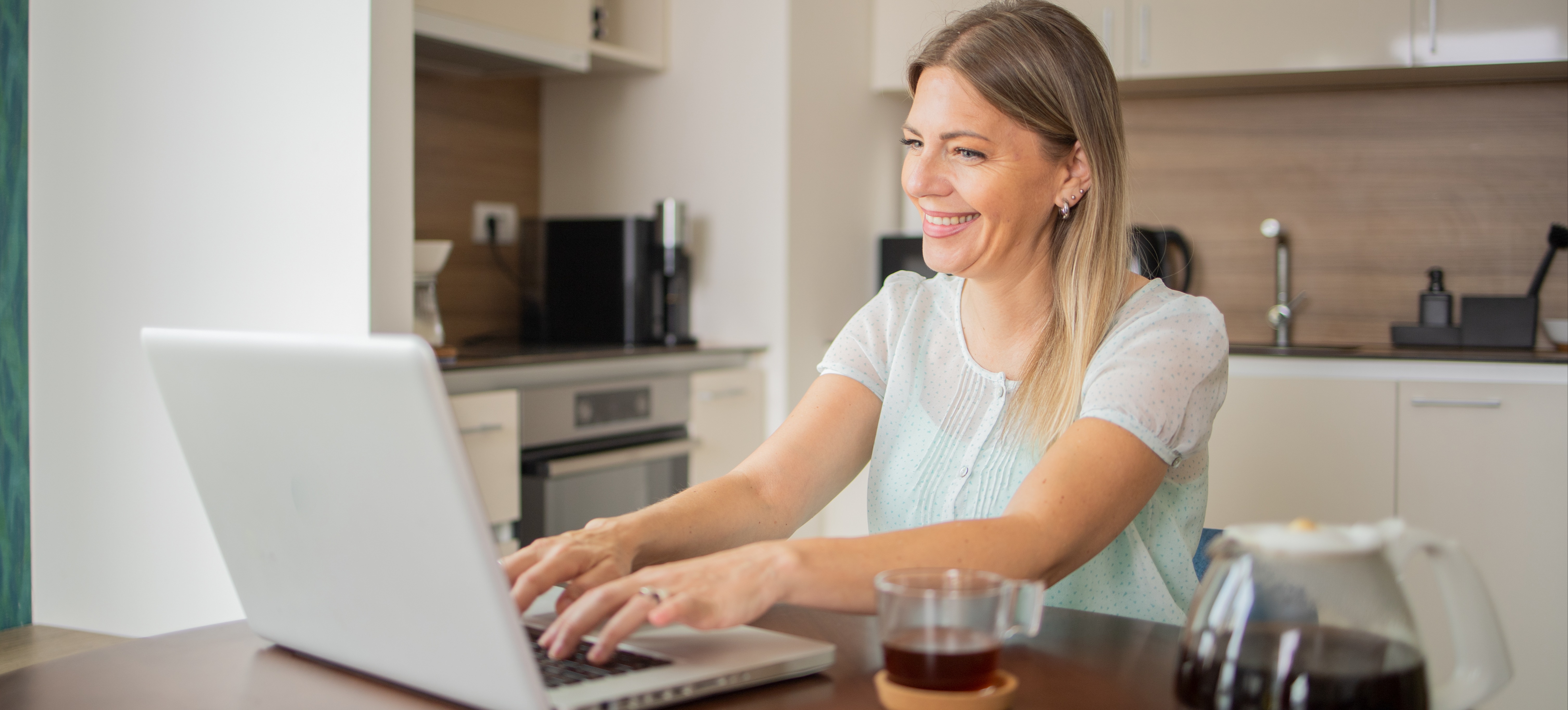 [Featured Image] A person sits in their kitchen and uses their laptop to research whether they should earn IT certifications or a degree for their career path. 
