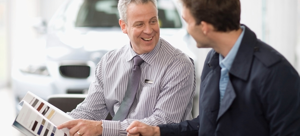 [Featured Image] A smiling sales representative wearing a tie points to a catalog and talks to a potential client.
