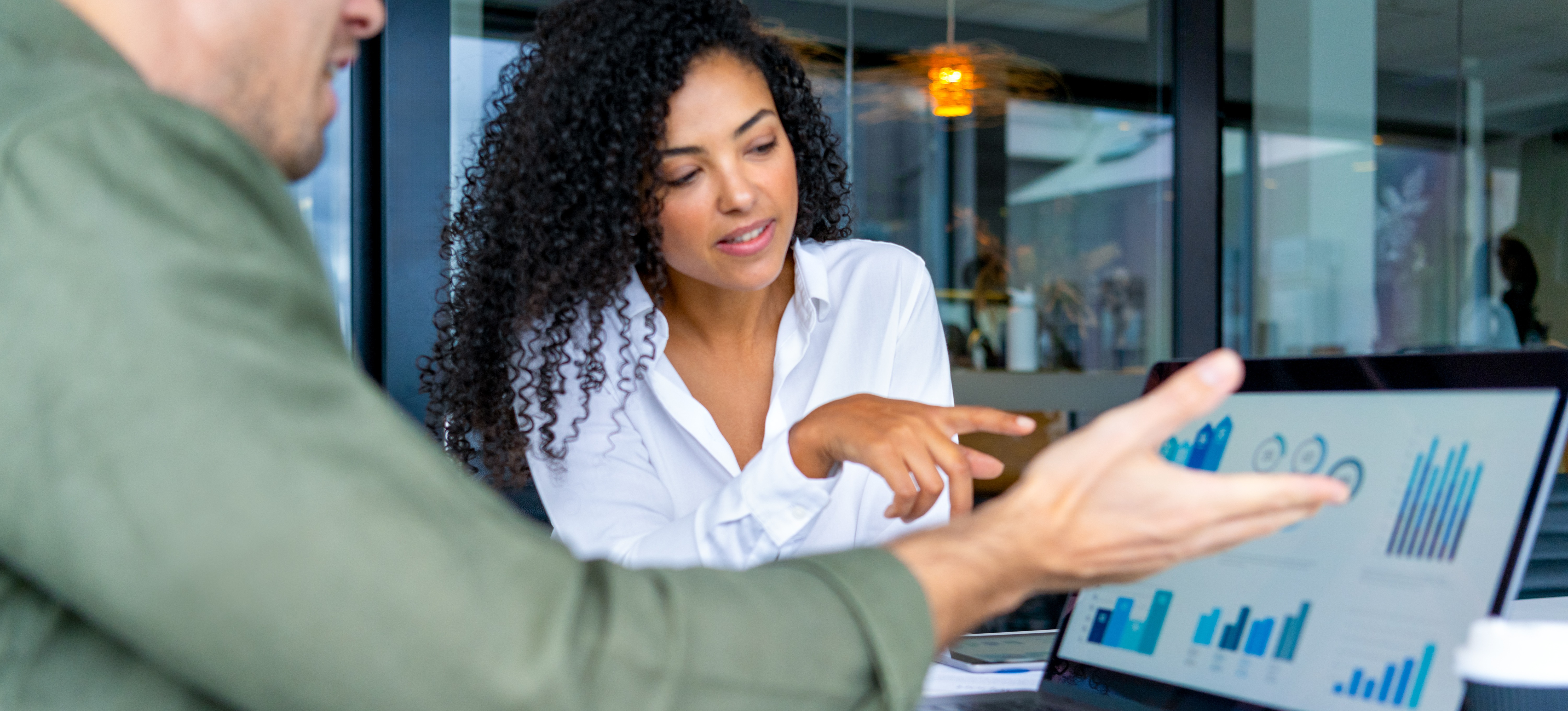 [Featured Image] Two professionals discuss financial econometrics while looking at statistics and data visualizations on a screen.

