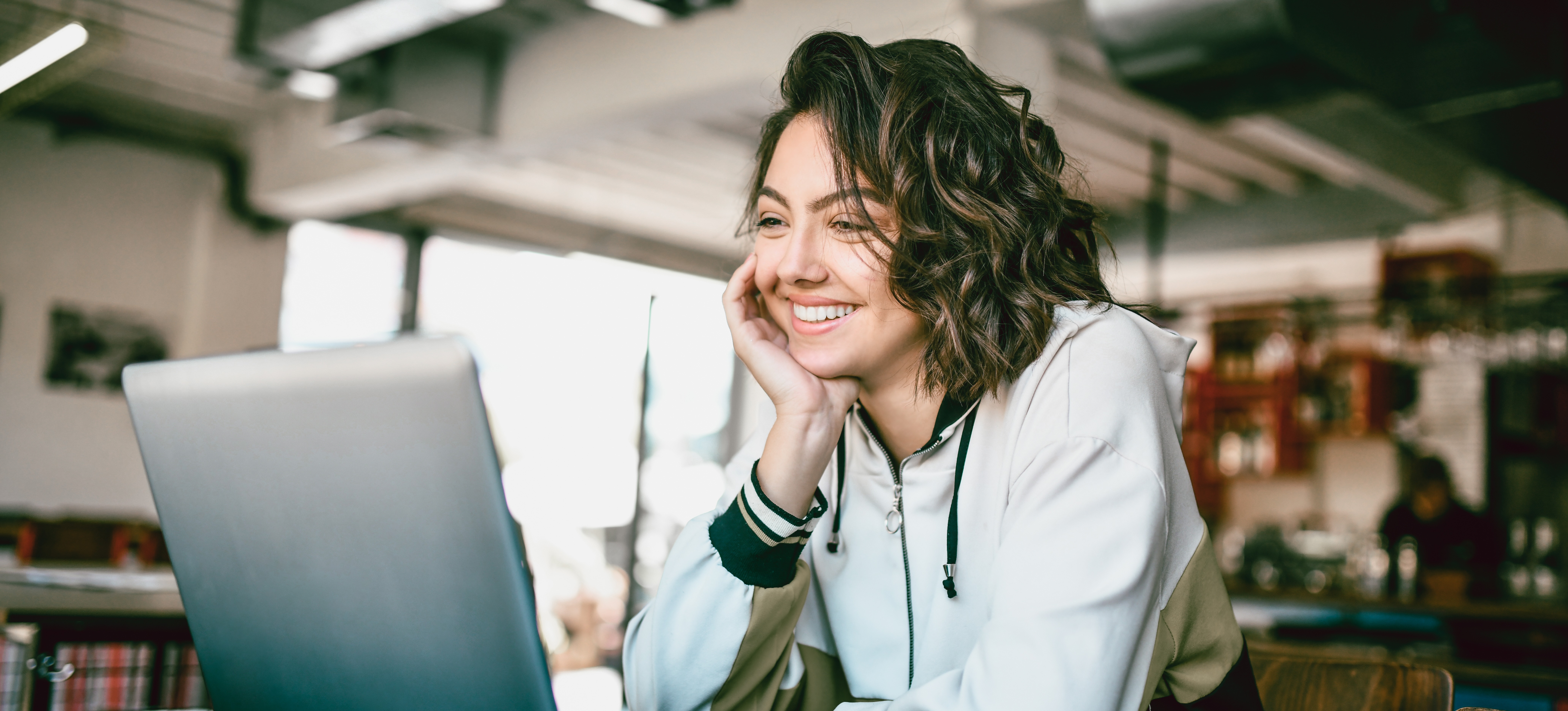[Featured image] A smiling digital marketer is reading an email created for email marketing on a laptop in an open office area.