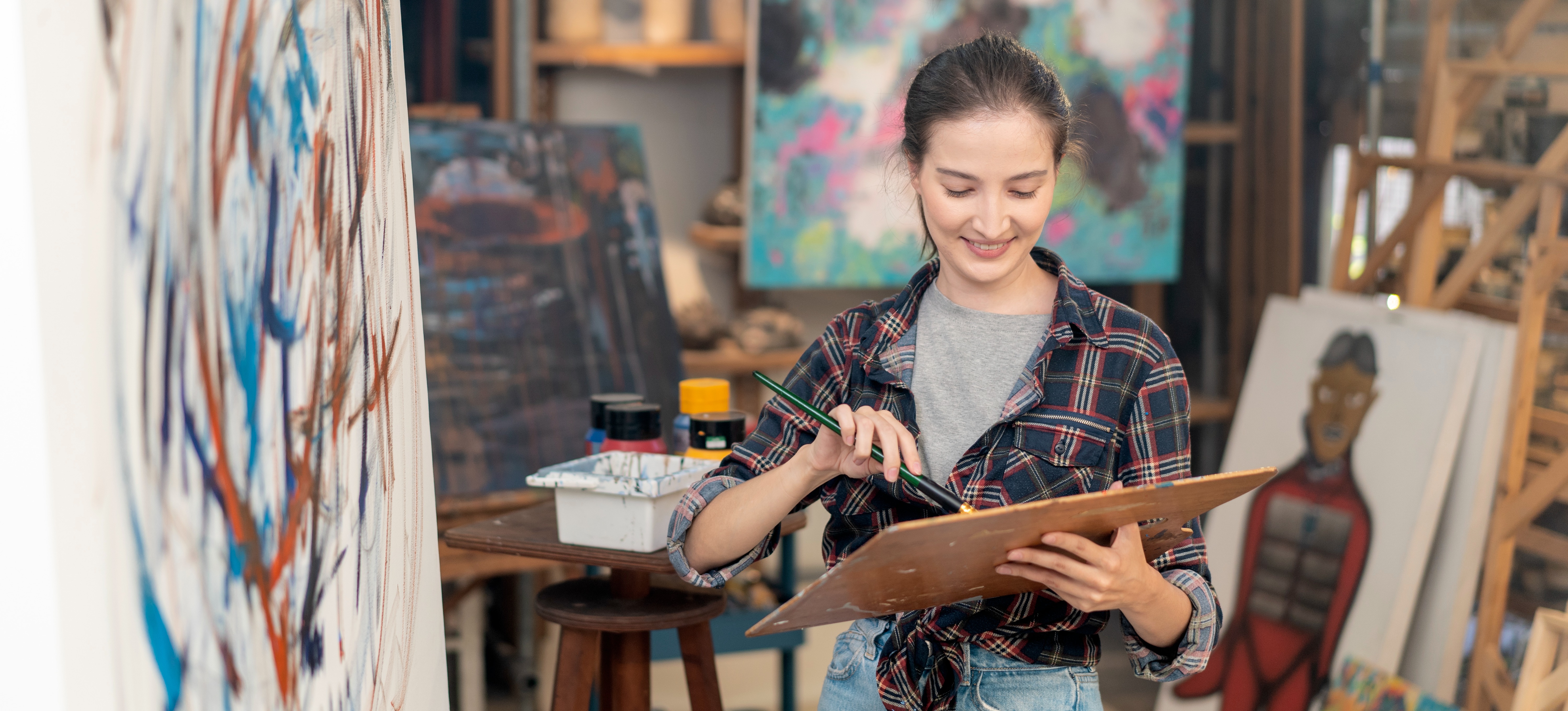 [Featured Image] A learner enroled in an MFA degree programme works on a painting in an art studio.