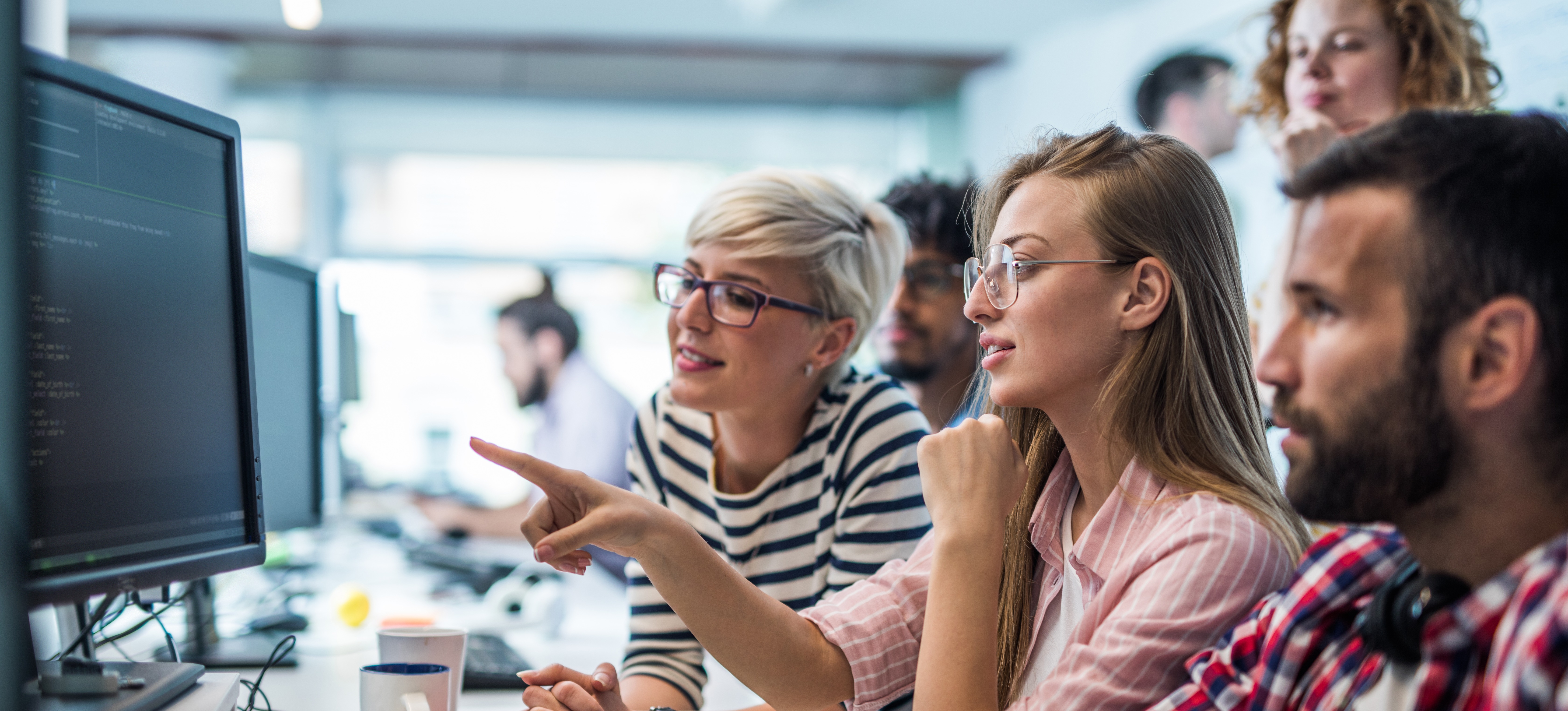 [Featured Image] Three web developers look at a computer monitor with django coding on it.
