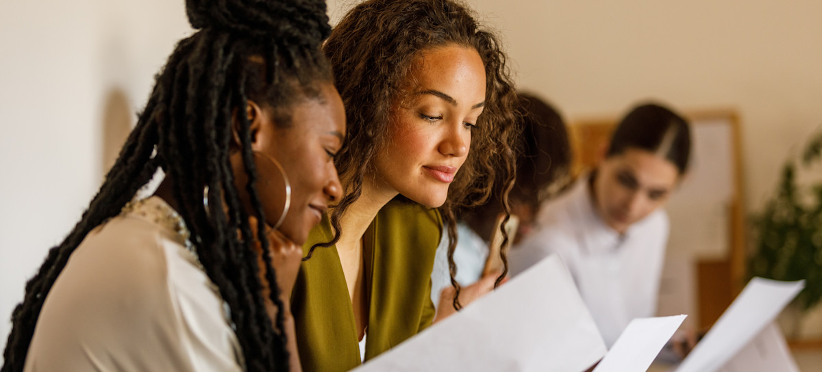 [Featured Image]: Business people sitting in line against the wall, chatting, preparing, and reading their resumes and cover letters when waiting for a job interview.

