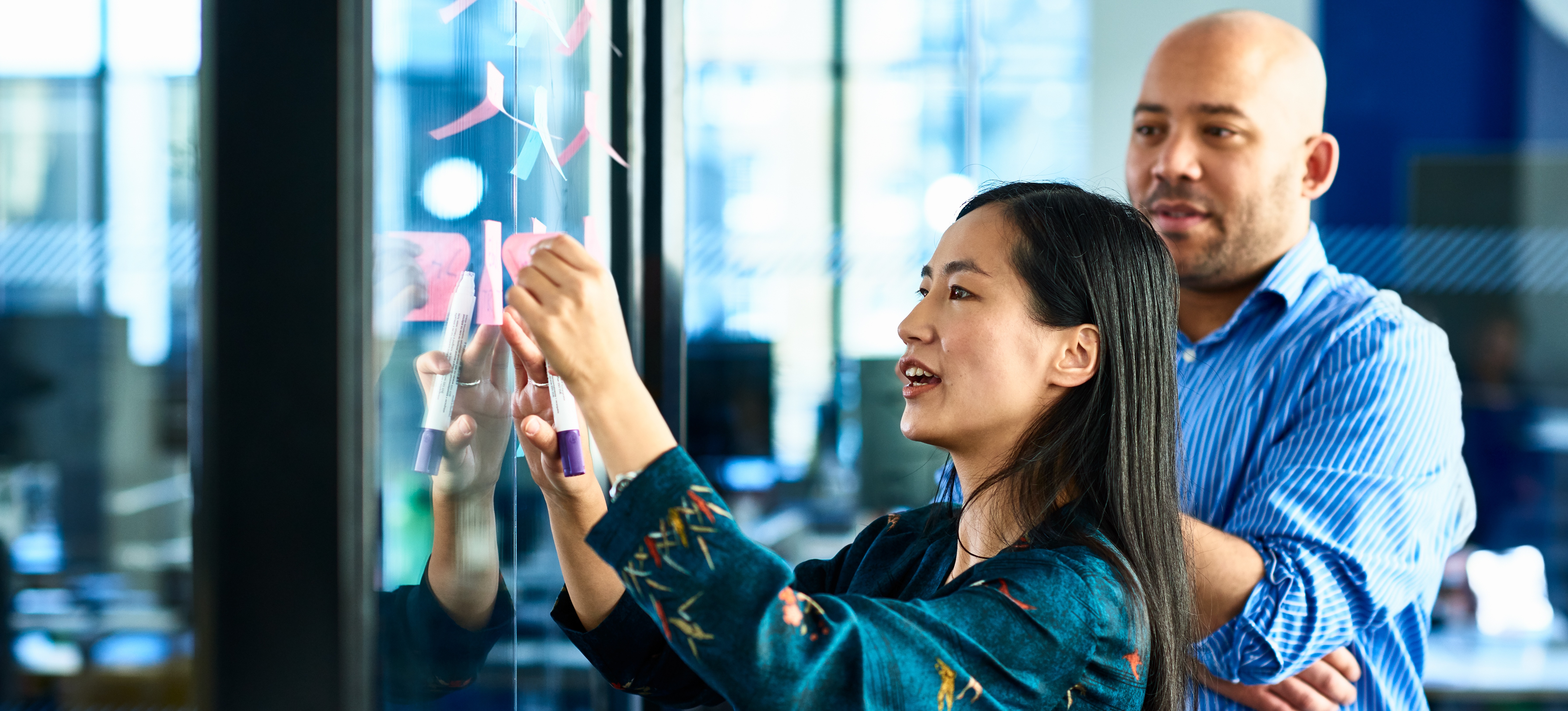 [Featured Image] An implementation manager is meeting with a colleague to discuss the steps and tasks to complete a project.