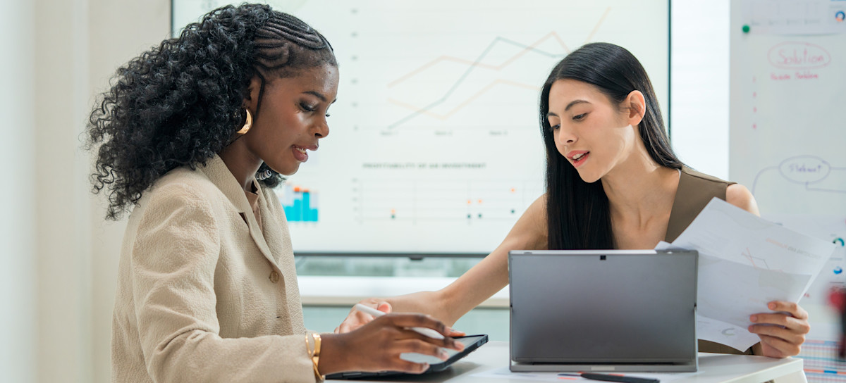 [Featured Image] Two learners work together to build their accounting skills as part of their educational pathway while studying in a classroom. 
