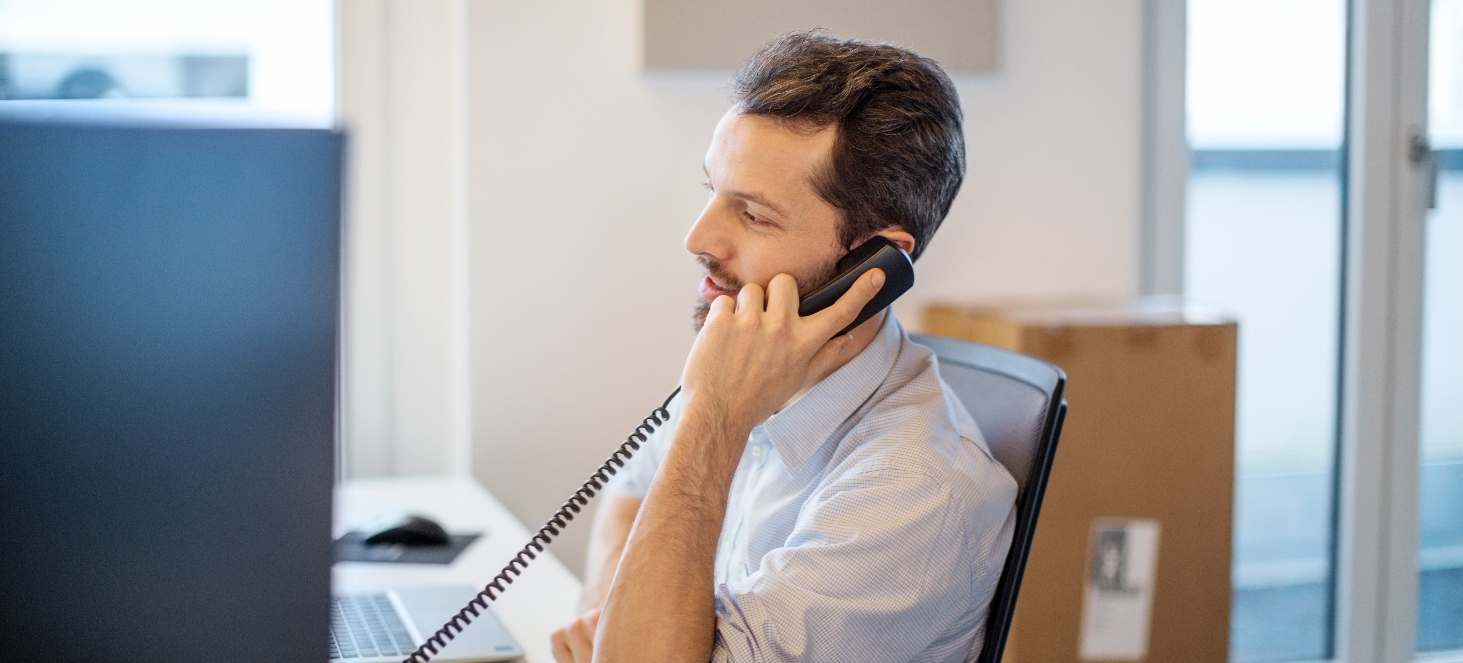 [Featured image]: Ein Versicherungsmathematiker telefoniert in einem modernen Büro, während er an seinem Computer arbeitet.
