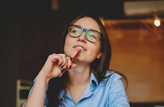 [Featured Image]: A woman wearing a blue blouse and glasses, with a pen to chin, thinking about her career path.