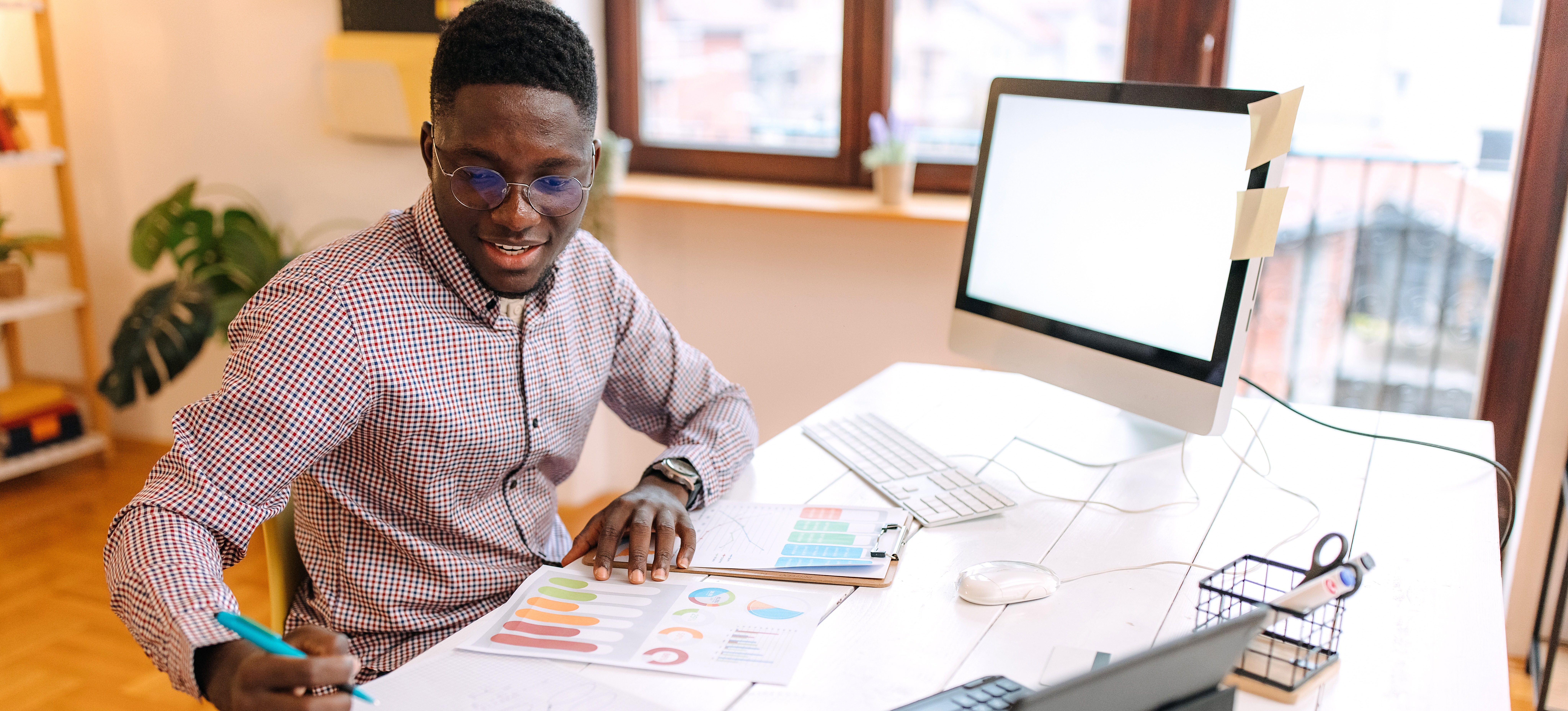 [Featured Image] A person is studying how to become a statistician while looking at graphs on their computer and paper printouts on their home desk.
