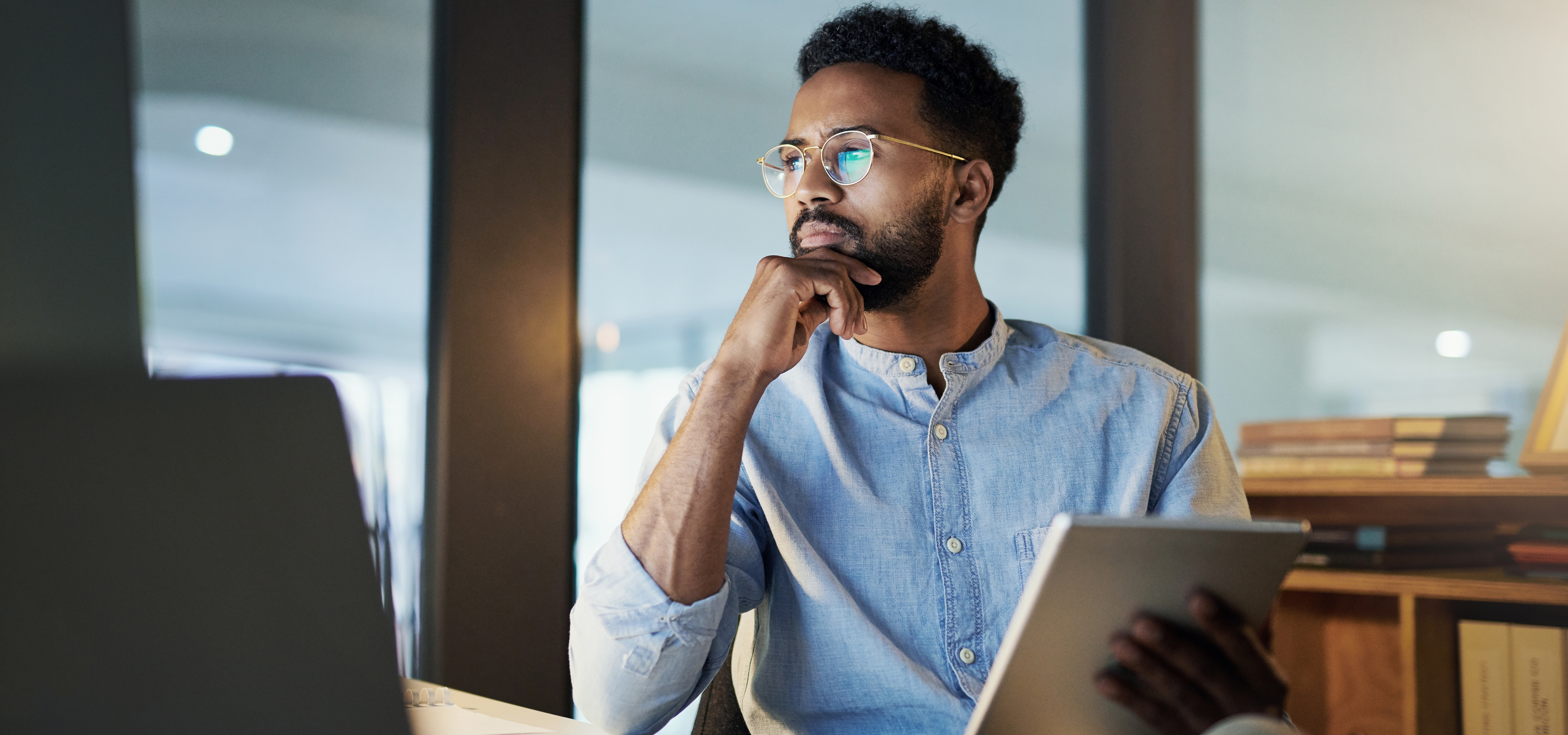 [Featured image] A person sits in their office preparing to do a cost-benefit analysis. They hold a tablet in one hand while looking at their desktop.  