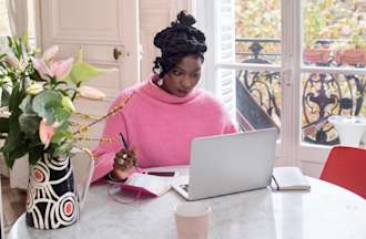 A woman works on her Google Ads campaign on a laptop while sitting at a table by a window.