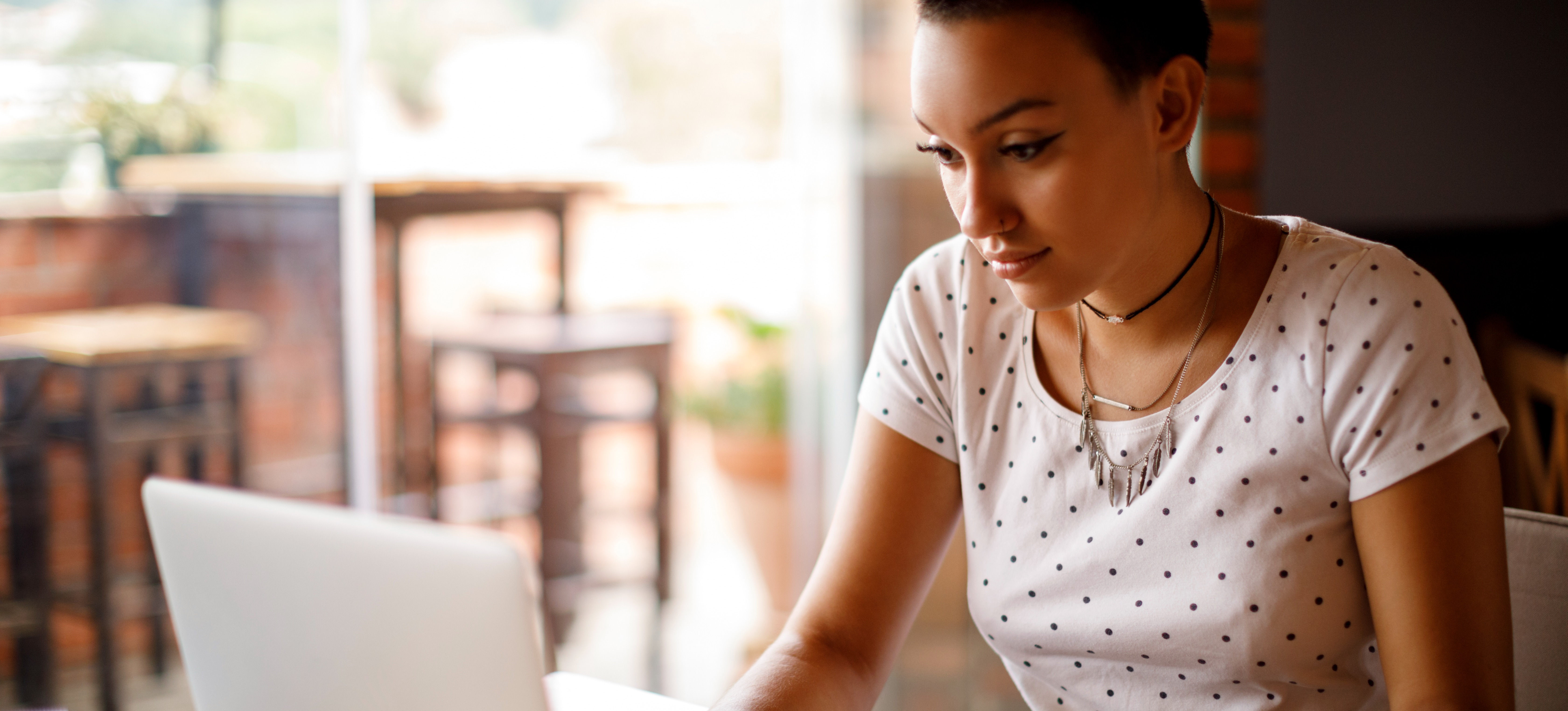 [Featured Image] A young college student working with a laptop and notebook at a cafe considers whether they should pursue an externship vs. internship.
