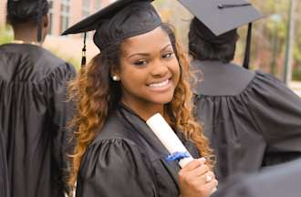 [Featured image] A woman in her cap and gown holds her diploma and smiles after getting her bachelor’s degree with her classmates.