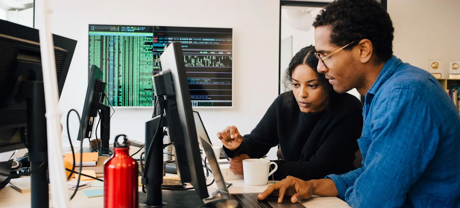 [Featured image] Two computer system analysts are working on a laptop, discussing their current project. 