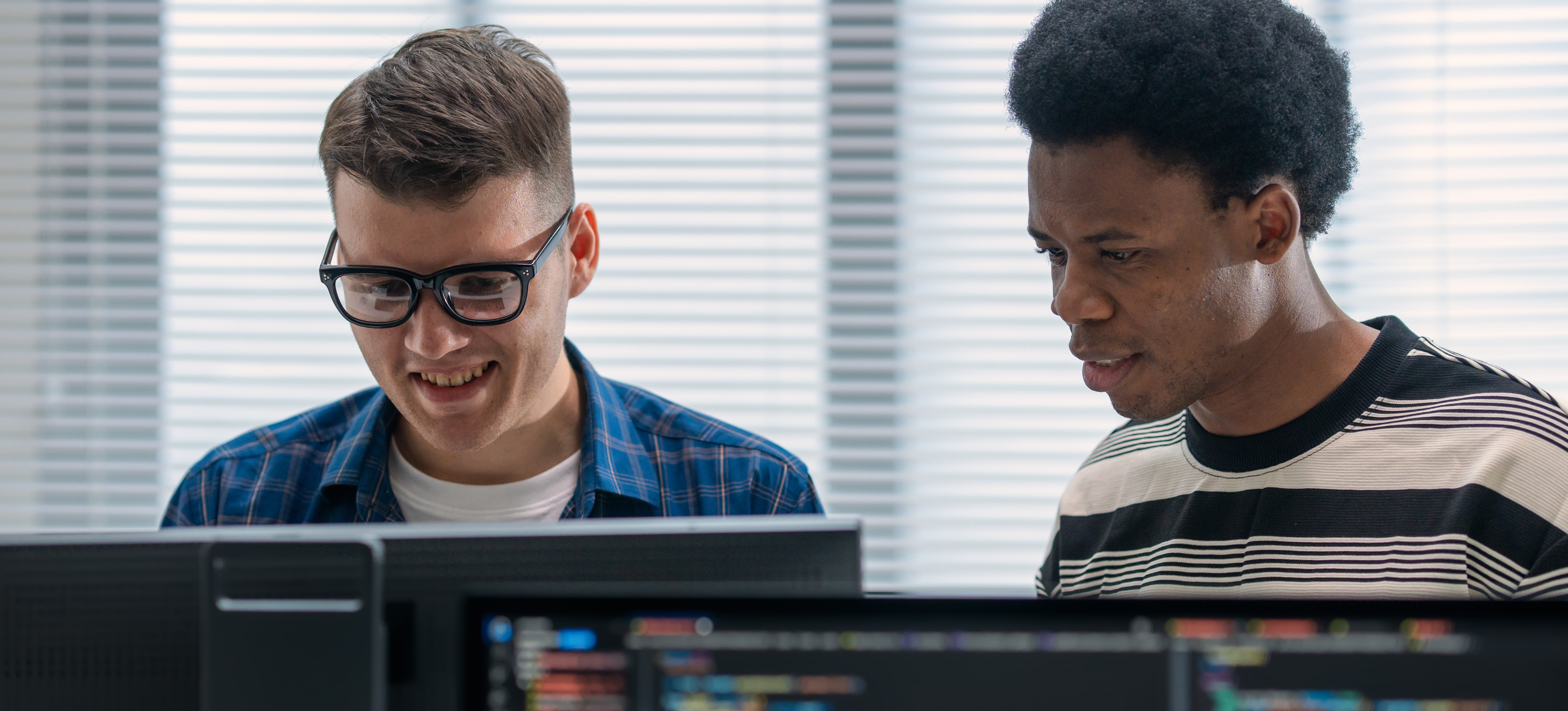 [Featured Image] AI practitioners in a workplace, interacting while AI-related code is displayed on the computer screen.