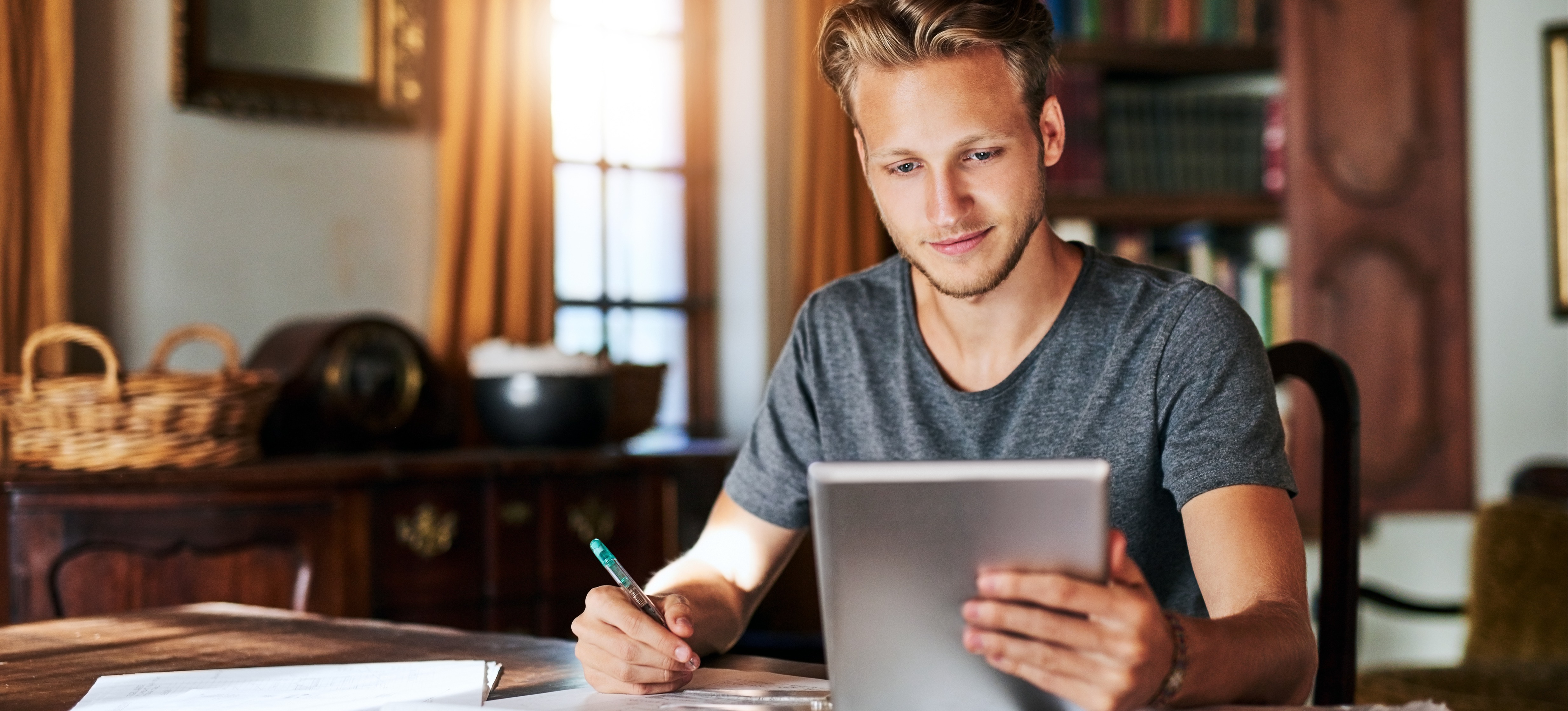 [Featured image] A learner sits at a table in their living room working on their MBA statement of purpose on a tabled and pen and paper.