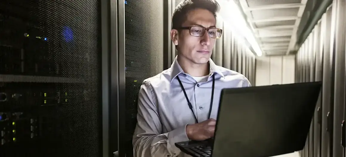 [Featured Image] An IT specialist uses ChatGPT for networking while standing in a server room and typing on a laptop.