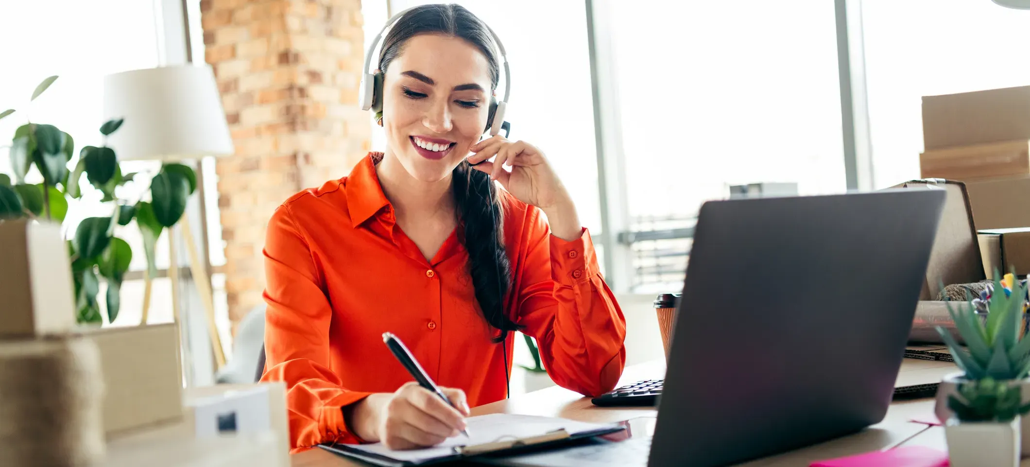 [Featured Image]: A person sits at a desk in front of a laptop, writes on paper, and talks on the phone about product marketing.
