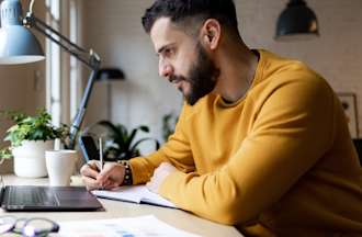 [Featured Image] A man who is looking for a new job sits at his laptop in his home and reads more about the cloud DevOps engineer salary and job outlook. 