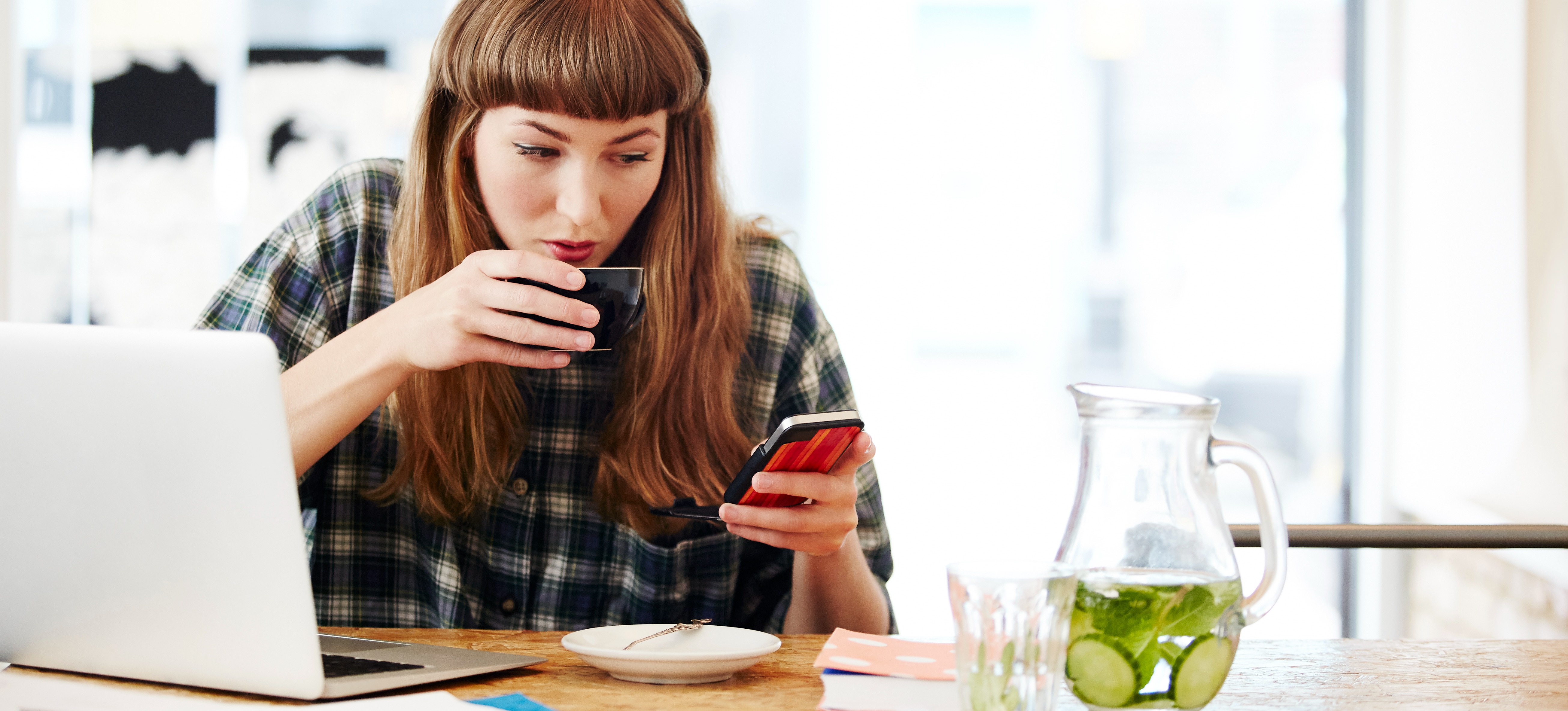 [Featured image] A person browses web pages on their phone and computer while drinking a cup of tea, looking for examples of paid media.