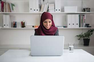 [Featured Image] A help desk technician smiles at someone on a video call in their home office. 