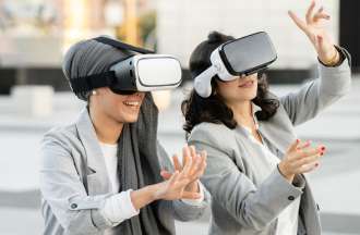 [Featured Image] Two businesswomen sit outside and use VR headsets that utilize VR eye tracking. 