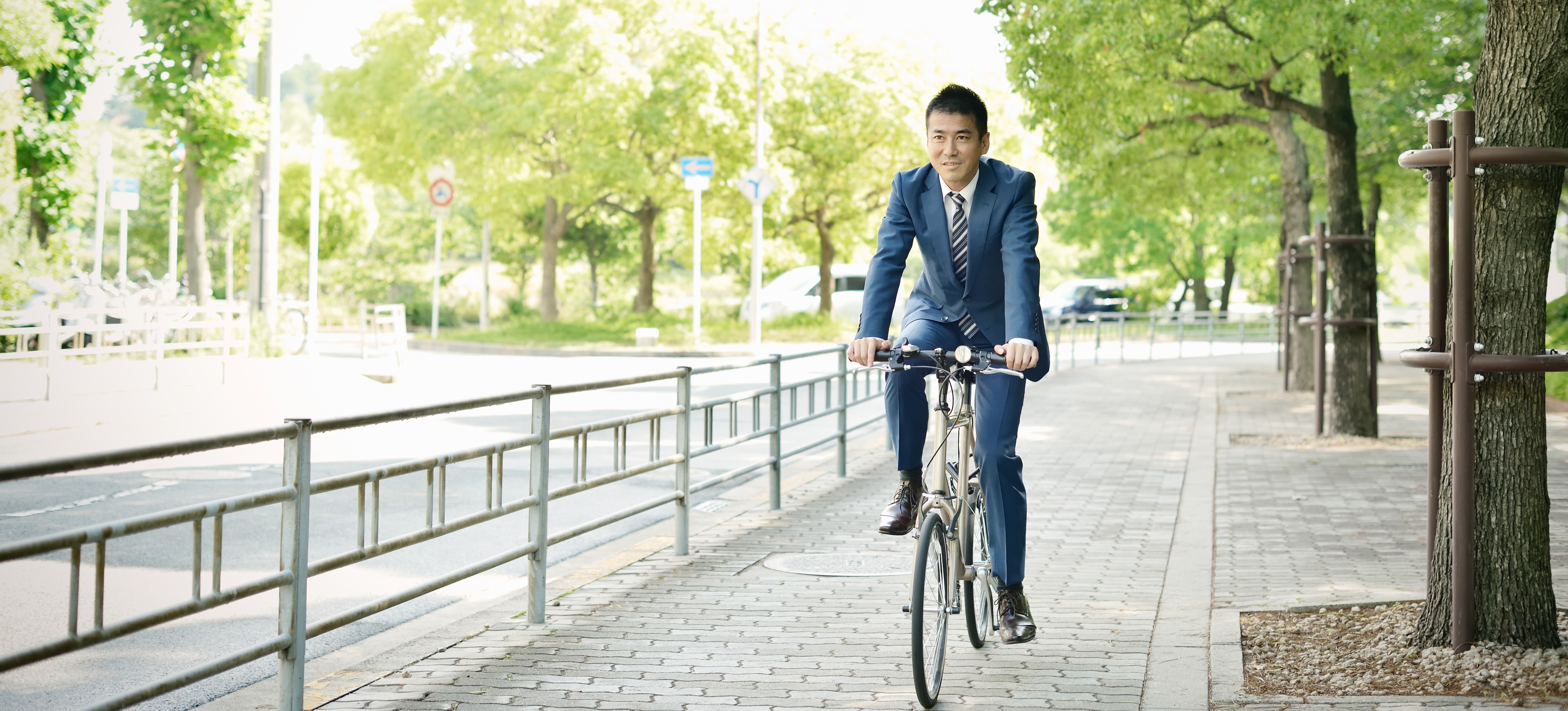 [Featured Image] A business person in a suit and tie rides their bike down a path on their way to their career job.