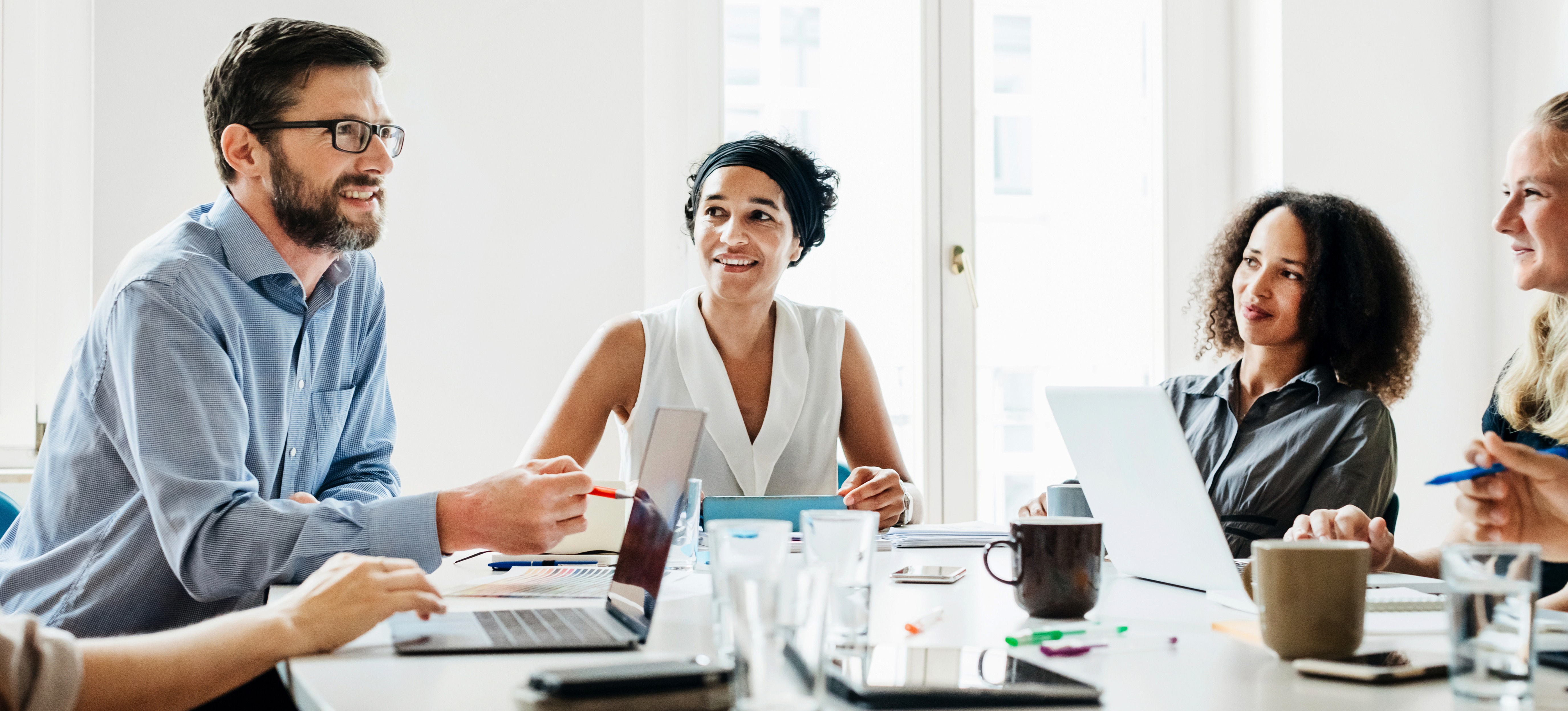 [Featured Image] A group of colleagues sit at a table and discuss the different types of operating systems and which one is best for their business.   
