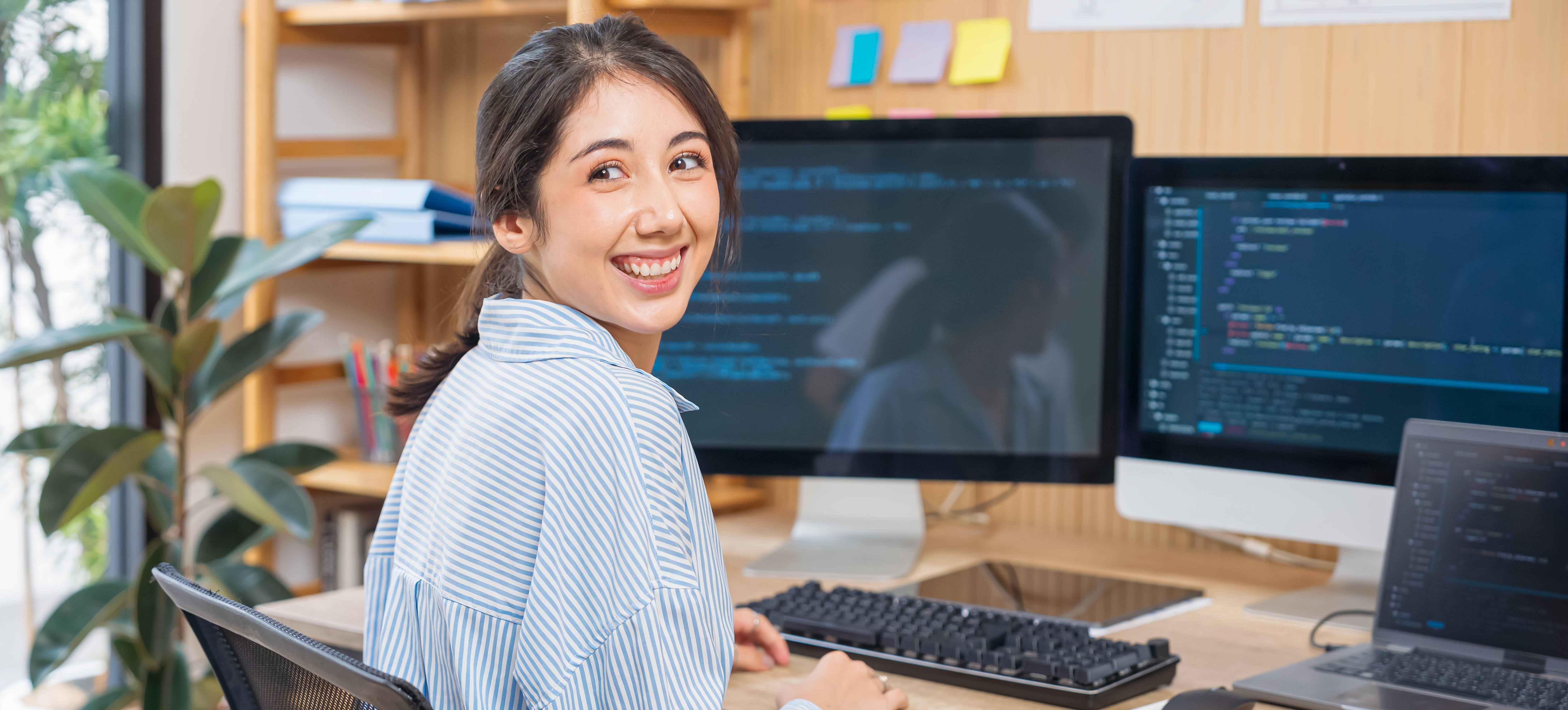 [Featured Image] A programmer smiling in a workplace environment, surrounded by computers, while working on AI-generated text and machine learning models.
