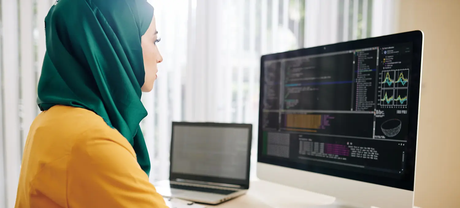 [Featured Image] A data engineer sits in front of a dual computer screen looking at data visualizations and writing in a notebook