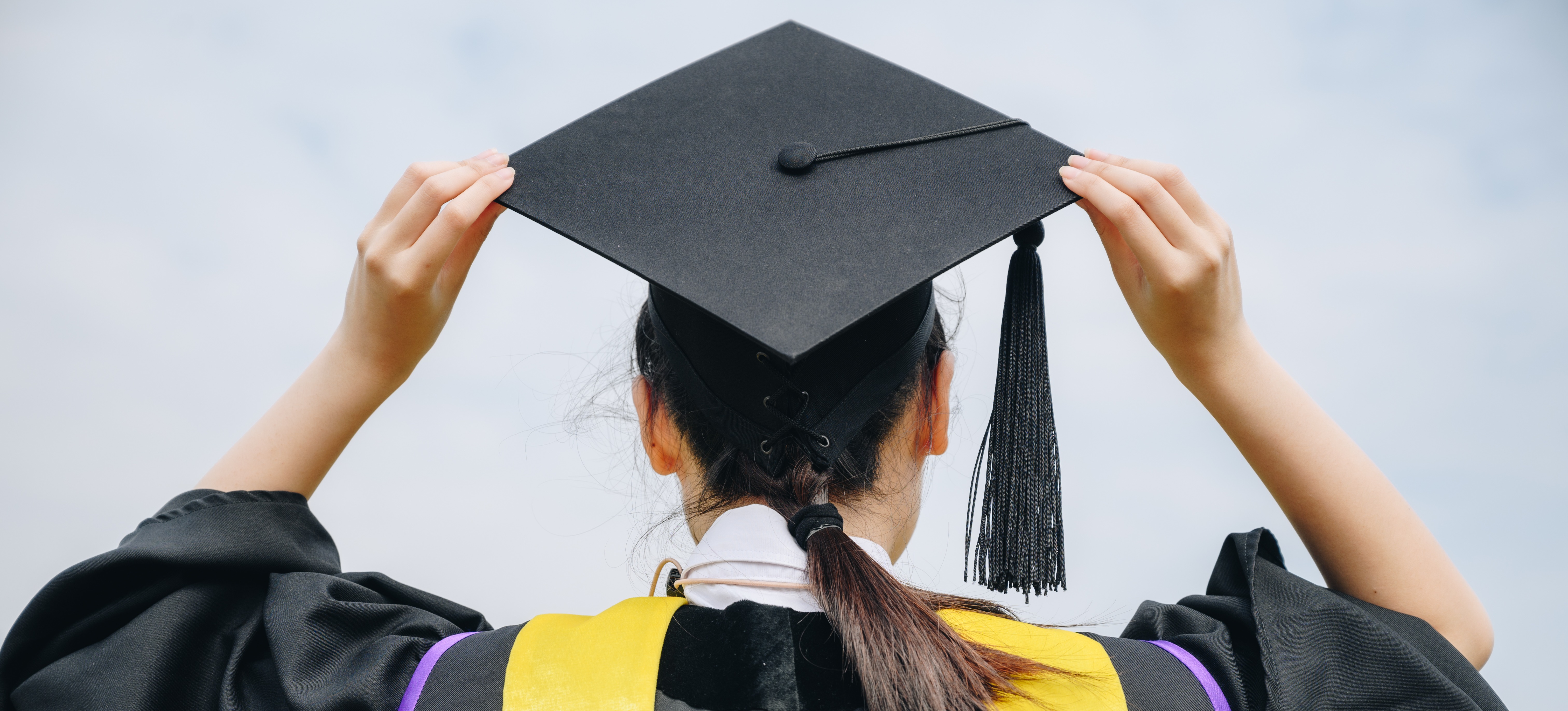 [Featured Image] A female college student is in a cap and gown excited to be graduation with a foundation degree.