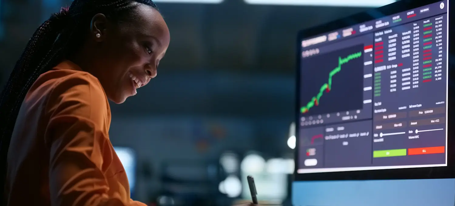 [Featured Image] A smiling data scientist analyzes data featuring outliers at their desk and has graphs displayed on their computer monitors.