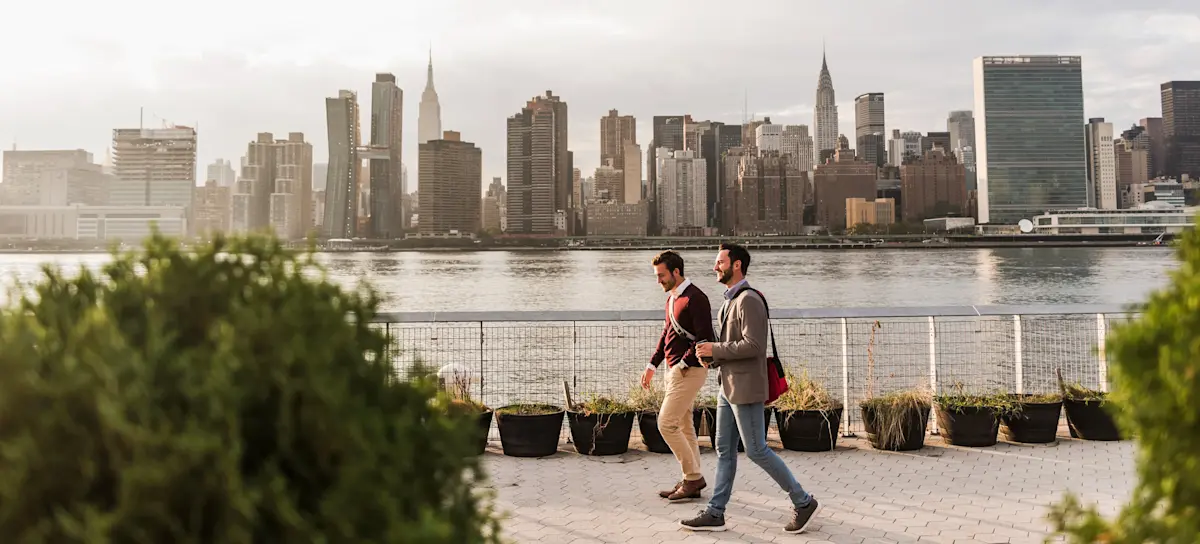 [Featured image] Two people in business attire walk along the waterfront with the New York City skyline in the background.