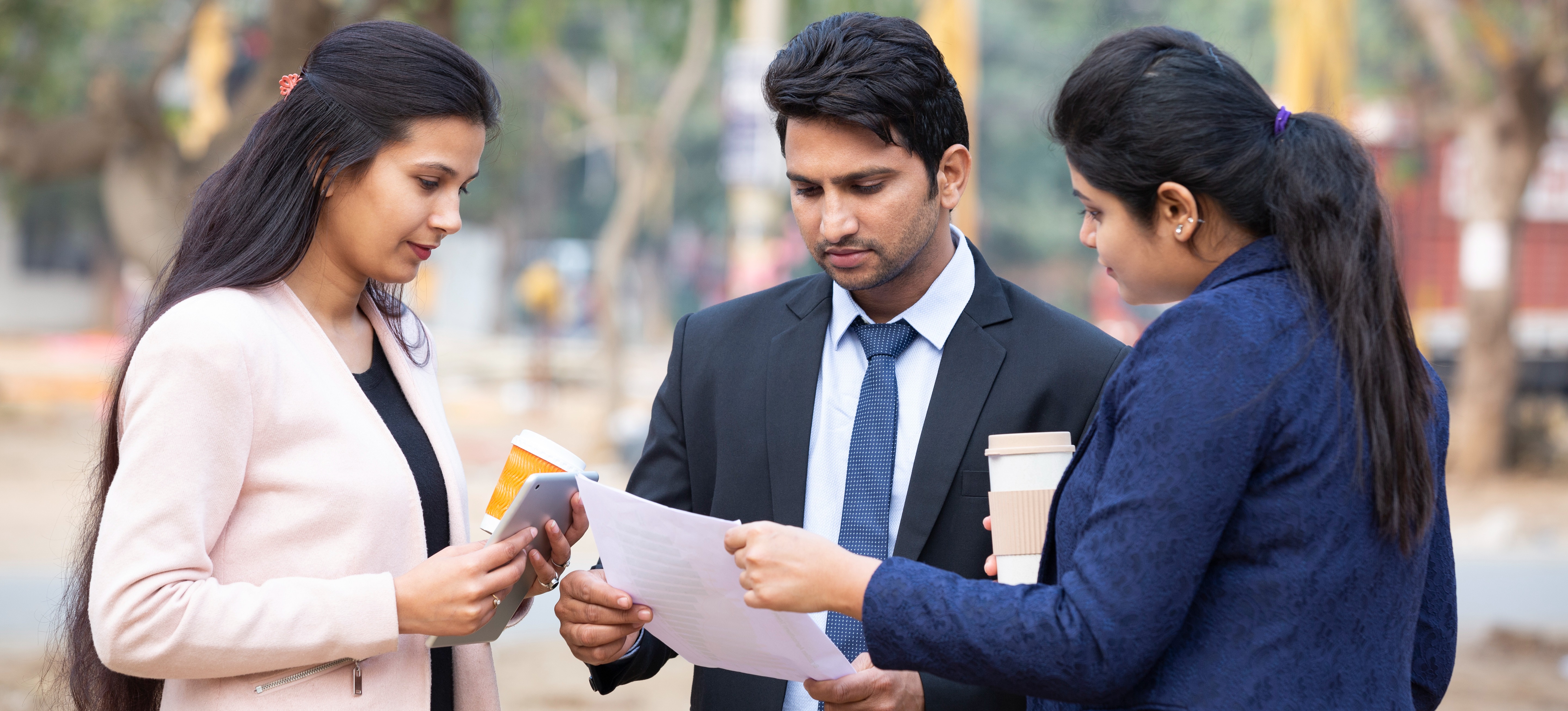 [Featured Image] Three colleagues dressed in business attire stand outside and drink coffee as they discuss the benefits of taking a PGDM course.