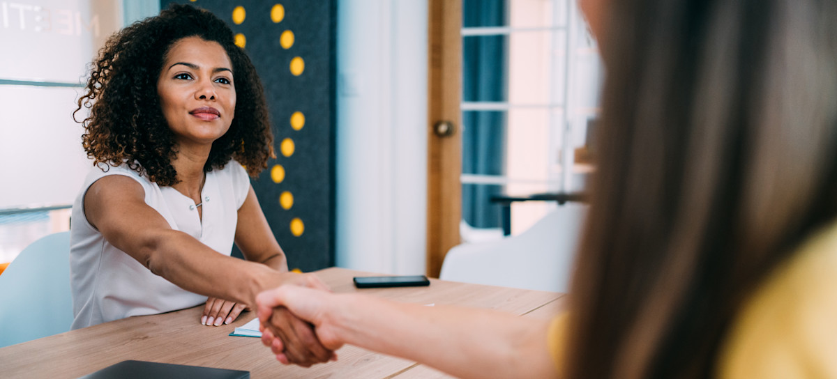 [Featured Image] A person working for an hr generalist salary shakes hands with a job interviewee across a desk.
