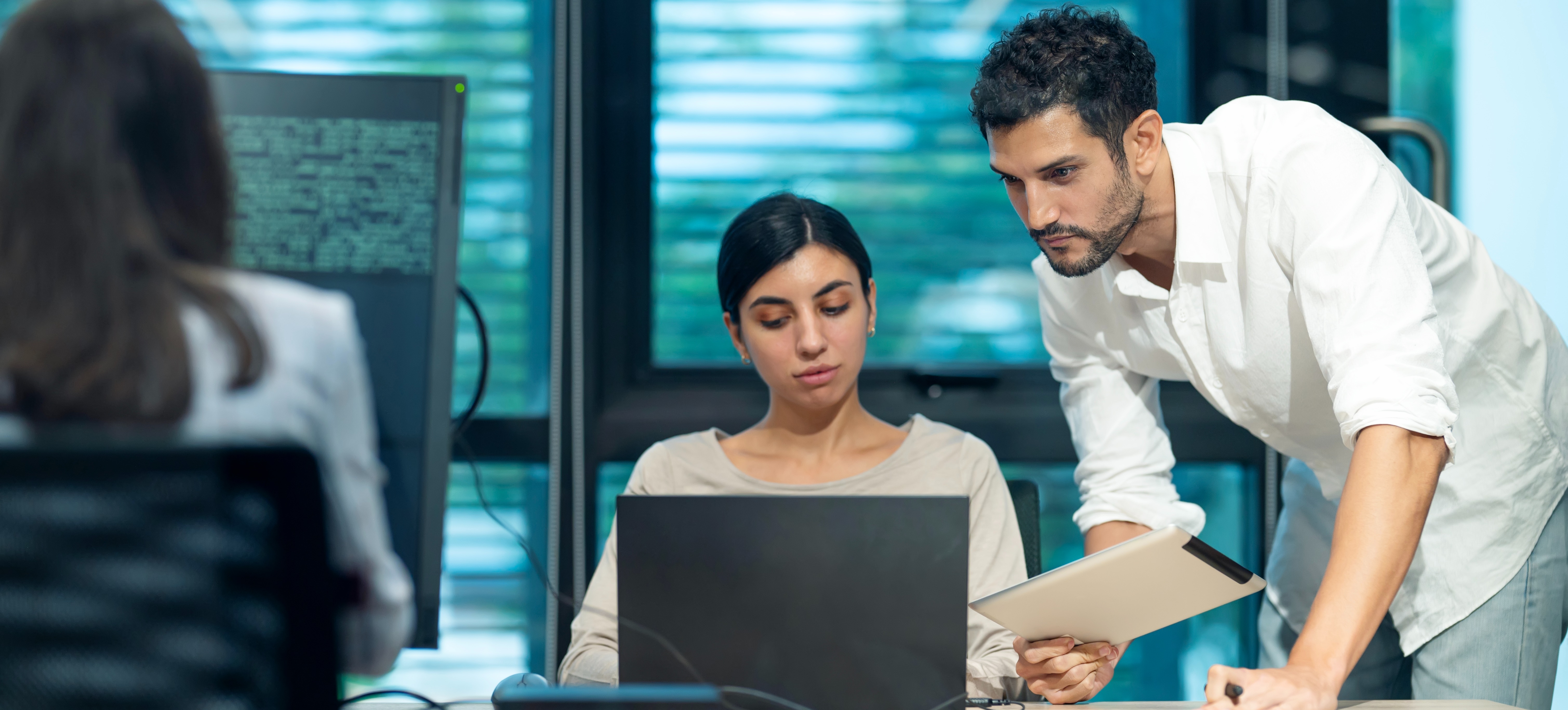 [Featured Image] A colleague explaining the concepts of cloud computing and edge AI to another colleague in a professional workspace, with a computer displaying code.
