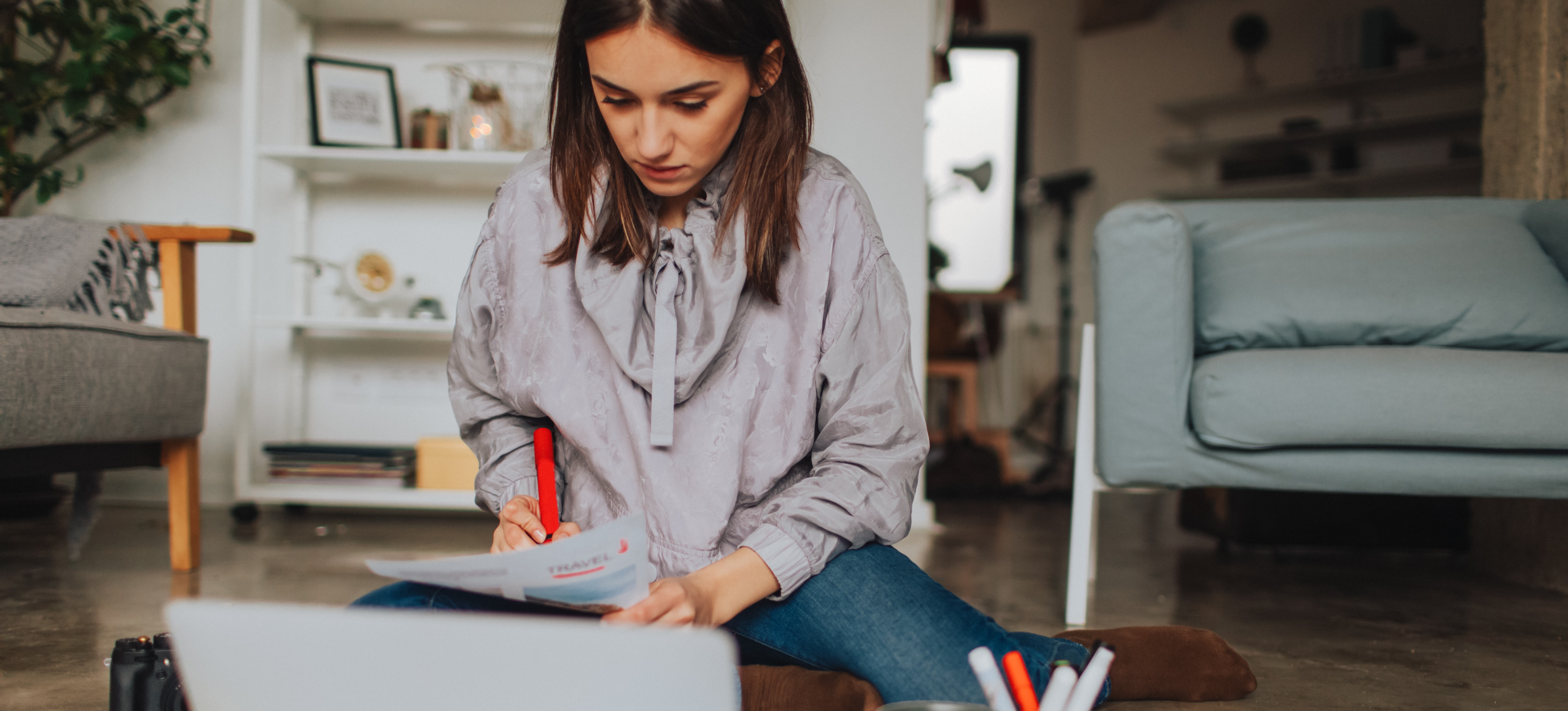 [Featured Image] A young woman who holds no marketing degree, is sitting on her livingroom floor, working on a marketing project for a company.