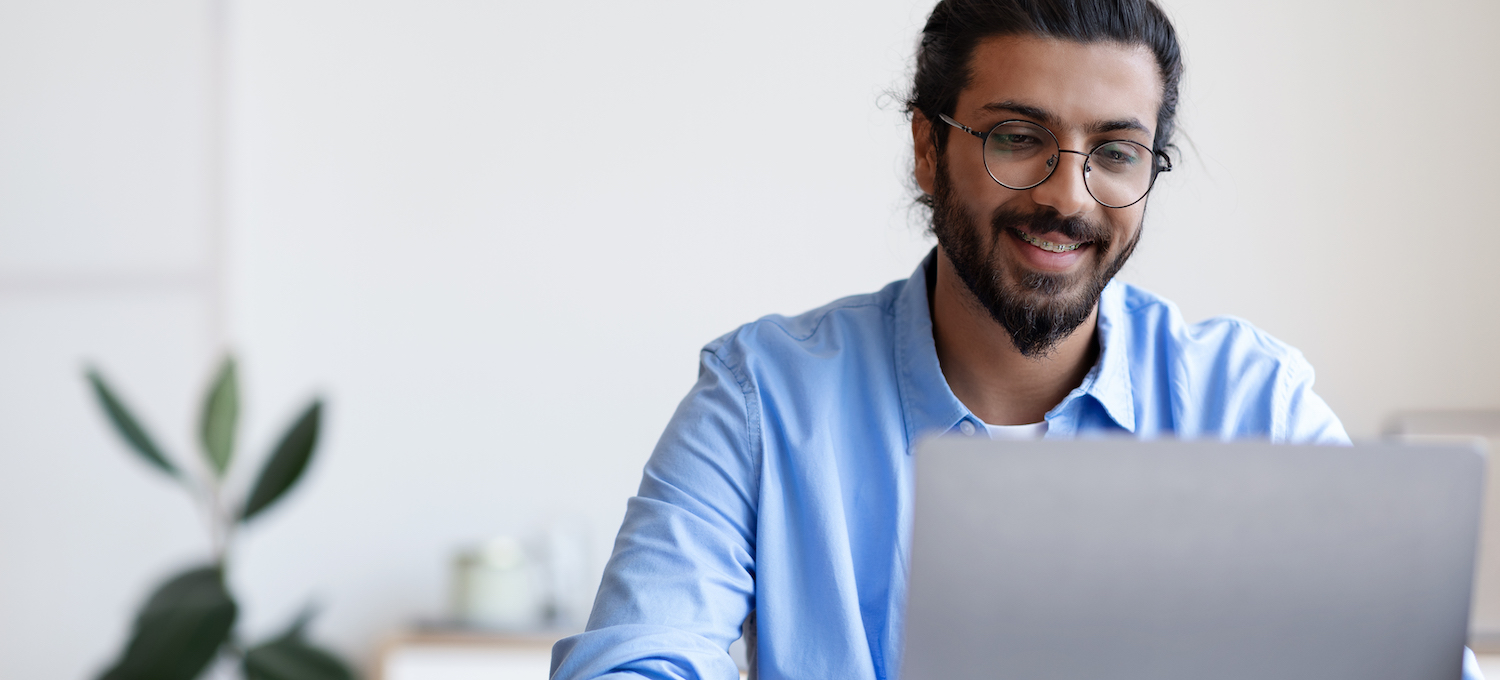 [Featured Image] A worker wearing glasses and a beard looks at a laptop.