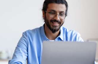 [Featured image] A young man with glasses and a beard looks at a laptop.