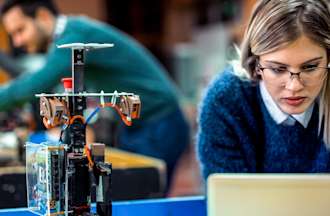 [Featured image] Blond woman wearing glasses and a blue sweater working in front of a computer at a futuristic computer science lab