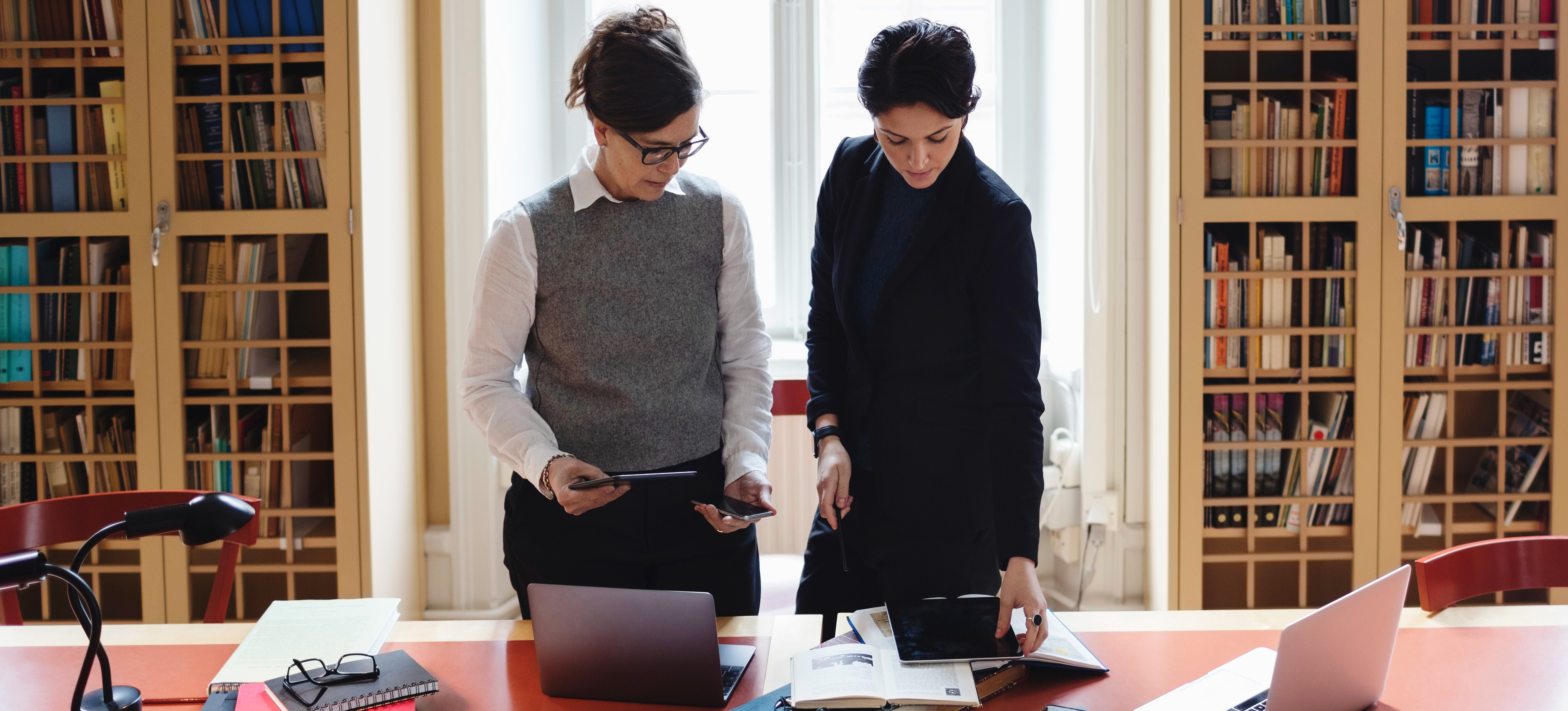 [Feature Image] Two people with an MSA degree stand in front of a conference table and review accounting numbers in a library.