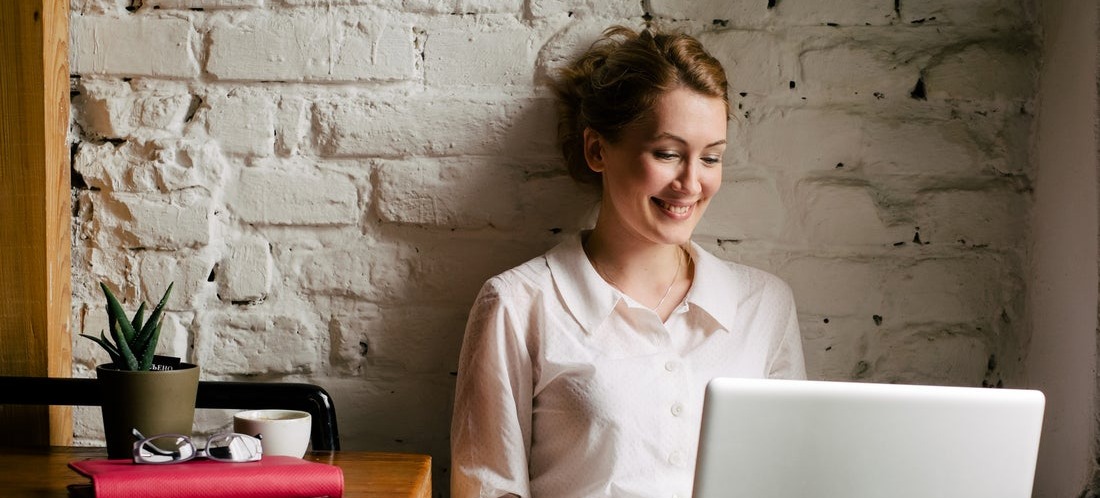 [Featured image] A happy woman smiles at her laptop as she updates her Shopify domain name for her rebrand.