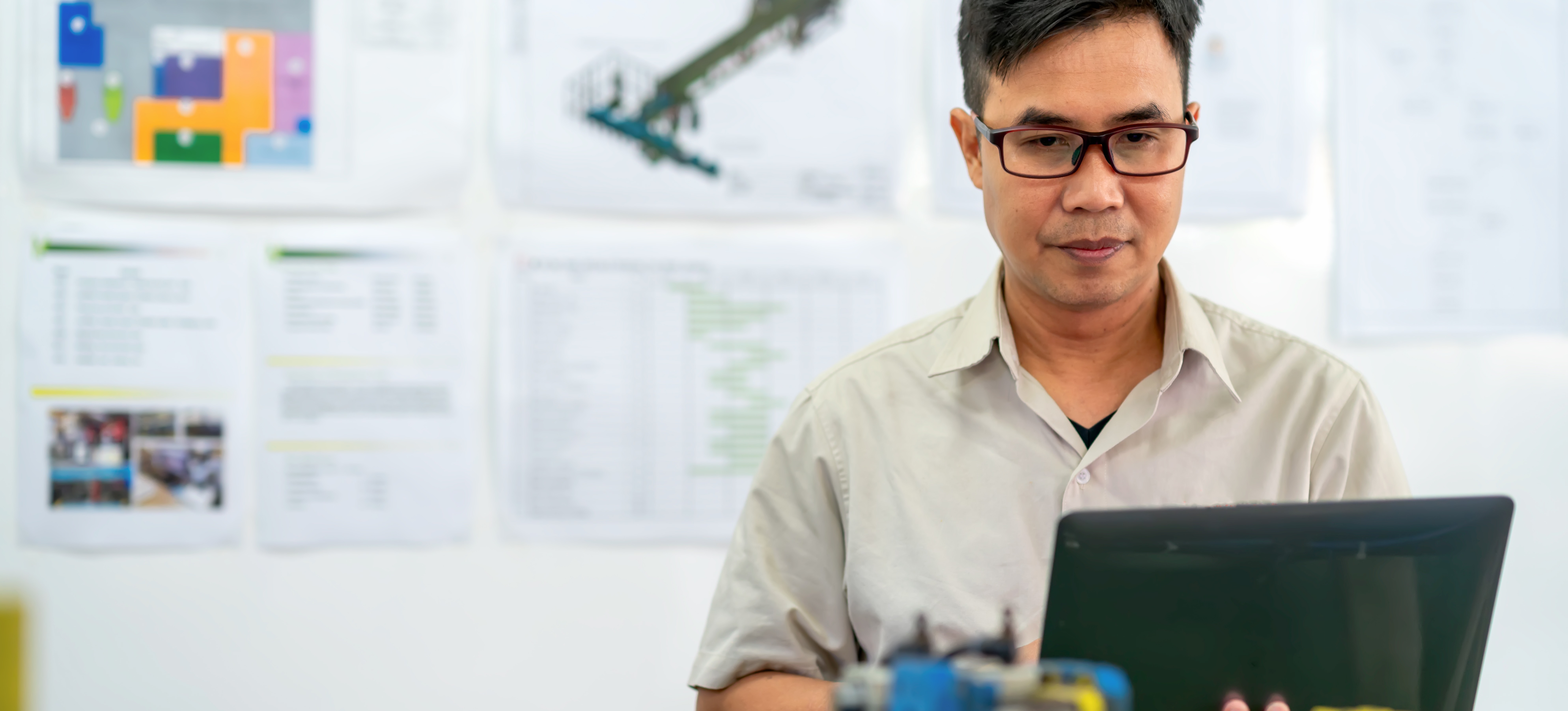 [Featured Image] A controls engineer examines their computer in front of a wall of mechanical diagrams.